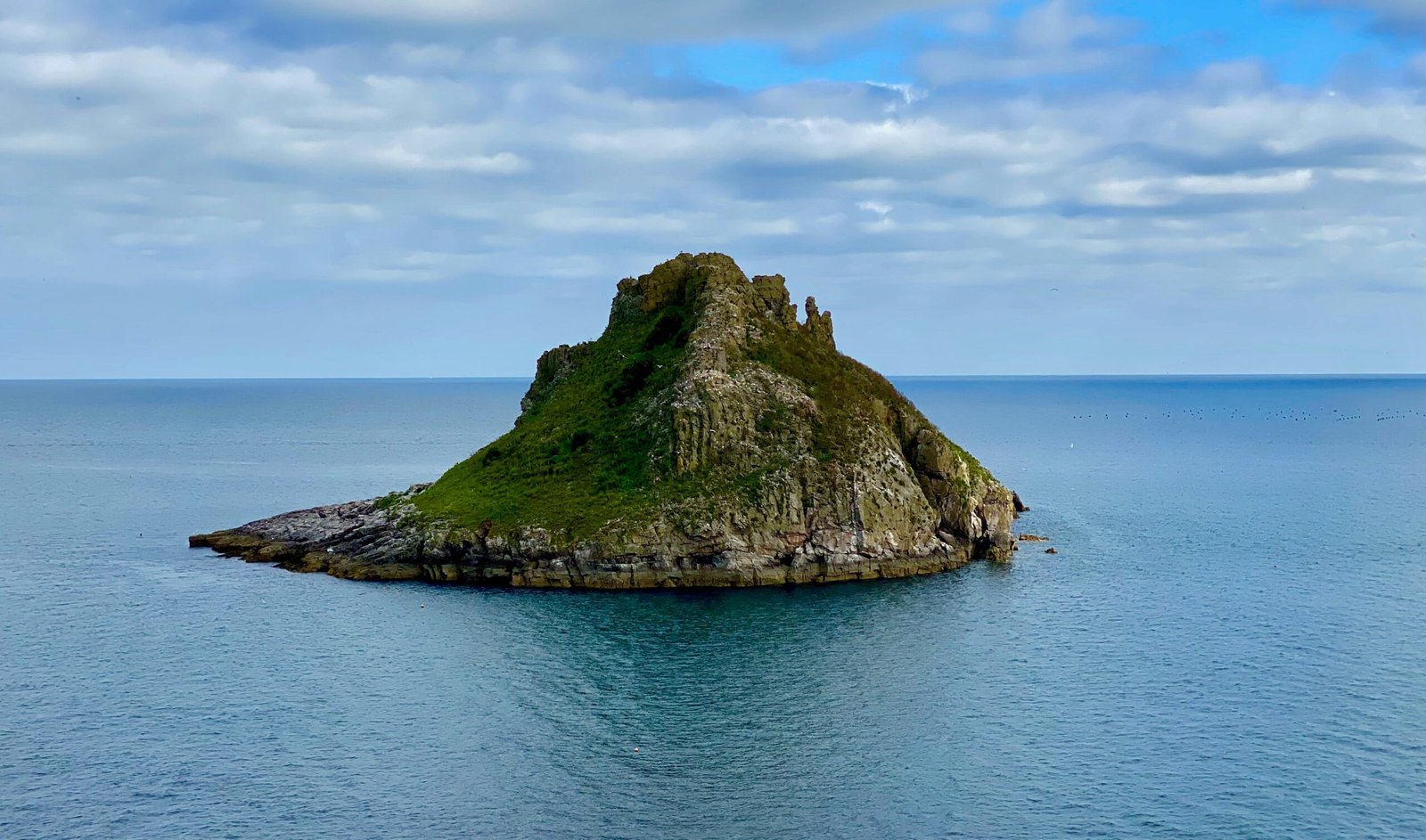 green and brown rock formation on blue sea under white clouds and blue sky during daytime